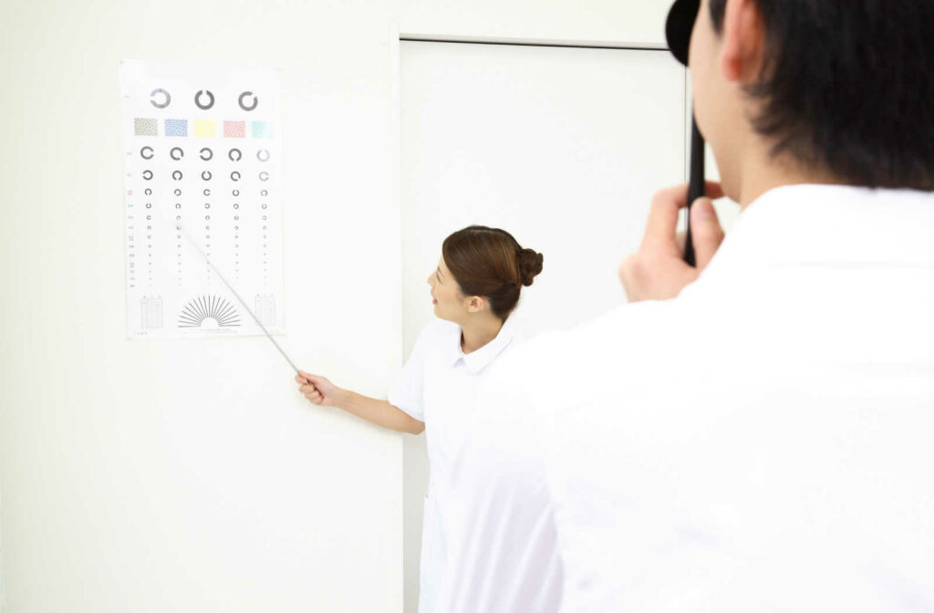 A female eye doctor is pointing at an acuity chart, while her patient is covering his eye and reading out loud the symbol he sees on the chart.