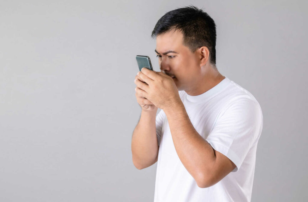 A man holding his smartphone with both hands close to his eyes.