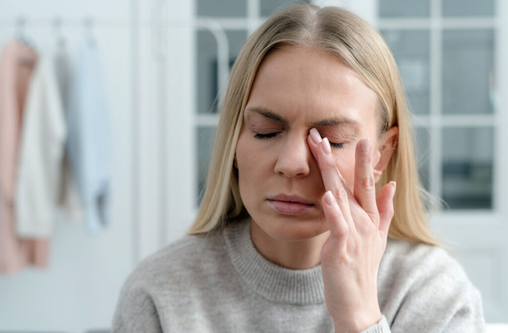 A woman in a grey sweater rubbing her left eye with her left hand.