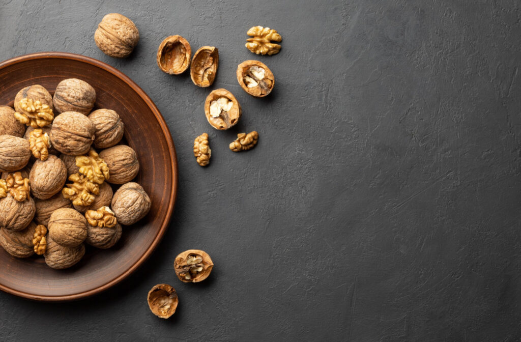 A wooden bowl filled with walnuts. Some cracked, some un-cracked.