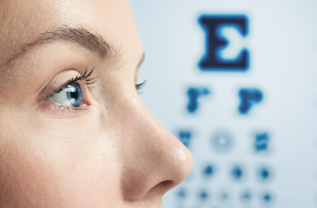 A close-up view of a woman's eyes and she is standing in front of a Snellen eye chart