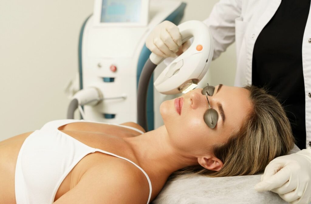 A woman lying on her back wears protective eyewear while a medical professional provides IPL treatment to her face