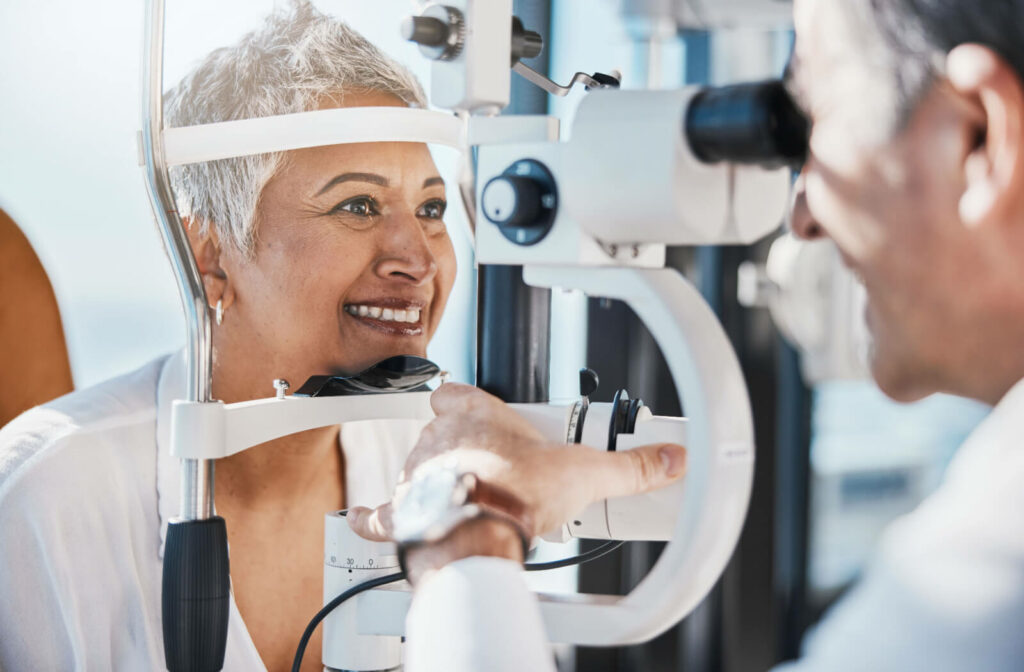 A senior woman smiling while her eyes are being checked during a routine eye exam.