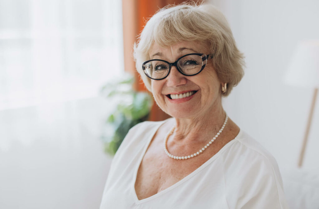 An older adult smiling in front of a window, showing off their new pair of reading glasses.