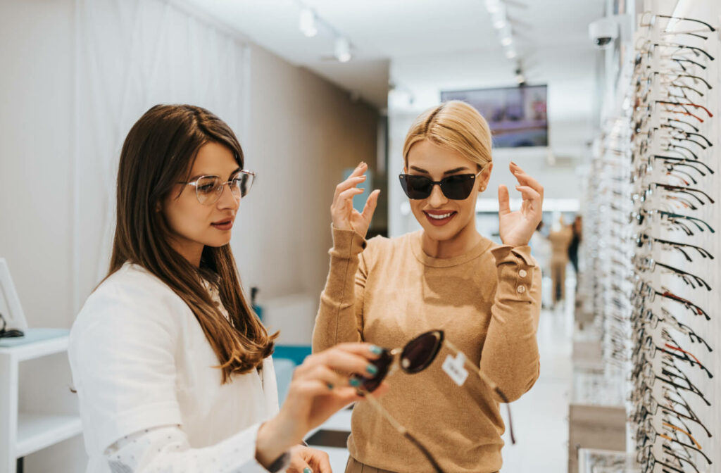 An optometrist helping an adult pick between polarized and non-polarized sunglasses in front of a display.