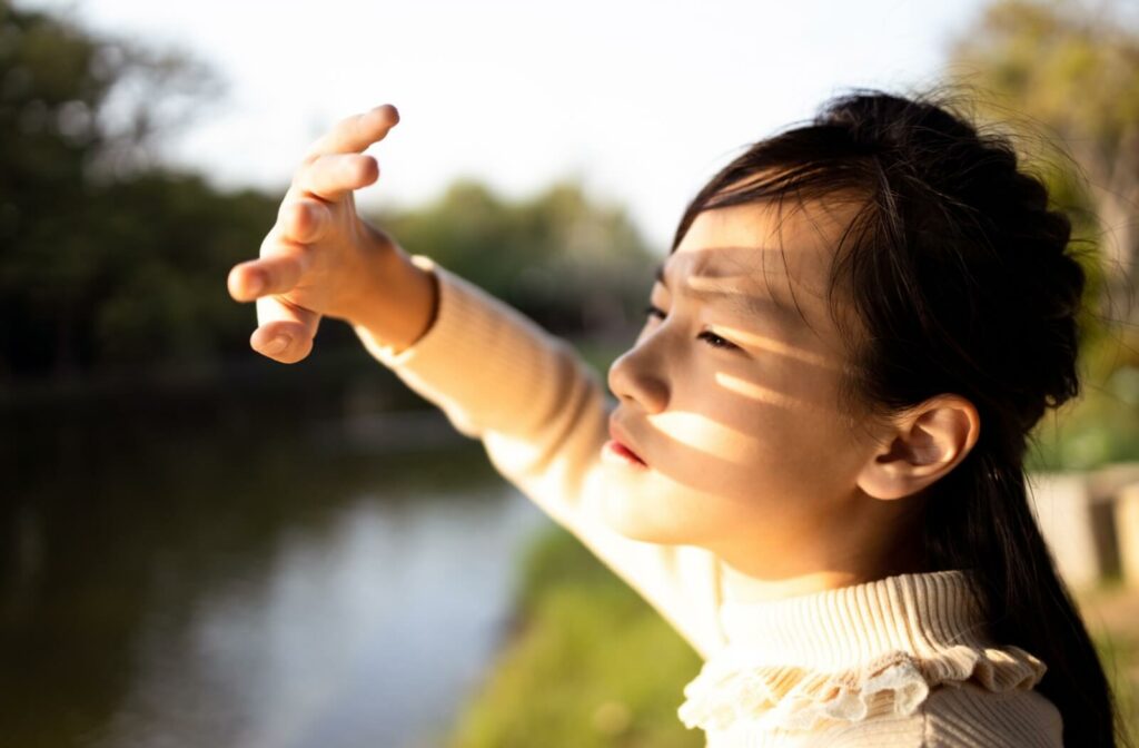 A young adult with dry eyes shields their eyes from the sun to prevent light sensitivity from bothering them.