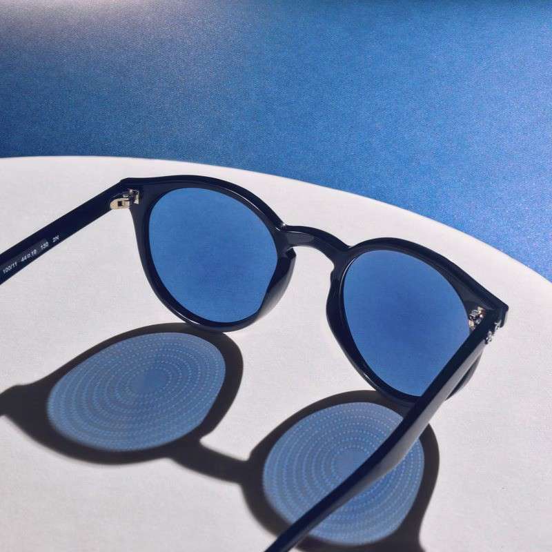 Pair of Stellest myopia-control glasses with blue lenses, showing the lenslet dot pattern clearly in the shadow cast on the surface.