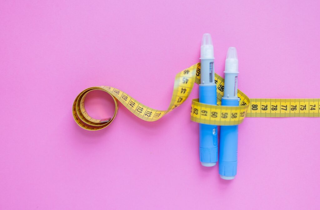 Two ozempic medication injection pens wrapped in a measuring tape, symbolizing weight loss treatments such as semaglutide.