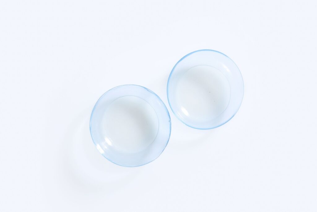 Two clear contact lenses displayed on white surface for vision correction.
