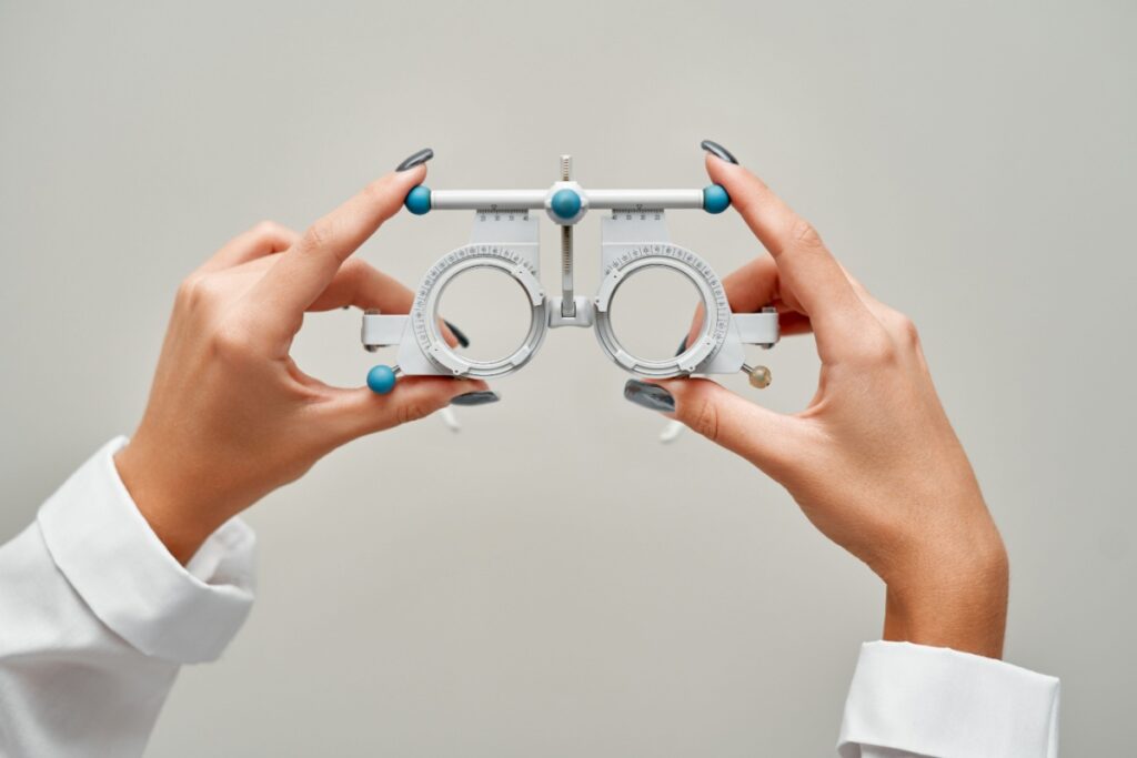 Optometrist hands holding up trial frames against a white wall.